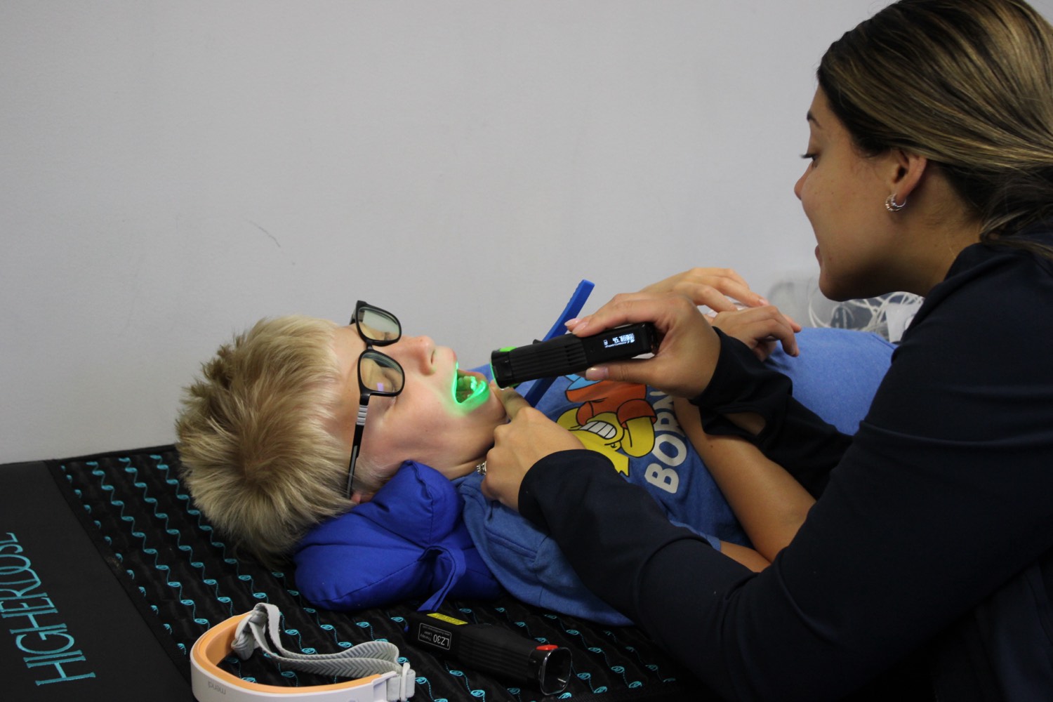 A Bright Beginnings therapist applies a handheld low-level laser during a gentle photobiomodulation session with a child resting comfortably